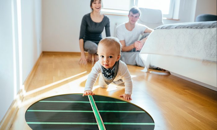 Couple sitting on the floor in bedroom with infant baby boy smiling and crawling to the camera. Happy family spending time tigehter at home in sunny day.